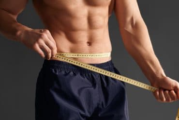 man with six-pack abs measuring his waist with a soft tape measure