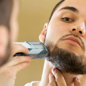 young man using an electric trimmer to clean up his beard