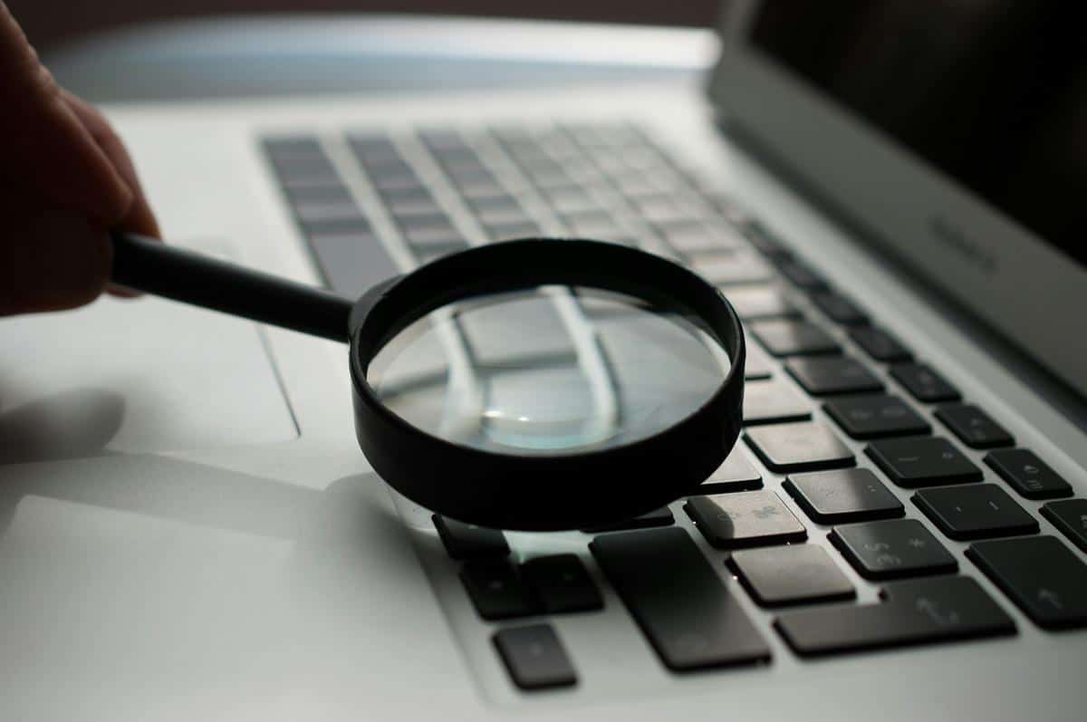 Image description: A magnifying glass placed on top of a laptop with multiple web pages on the screen, symbolizing the importance of an online presence for a side hustle.